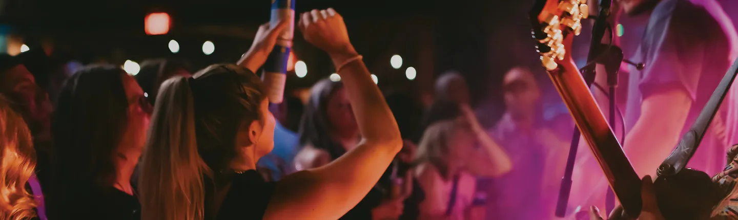 Crowd dancing near live band with guitar on stage under colorful lights