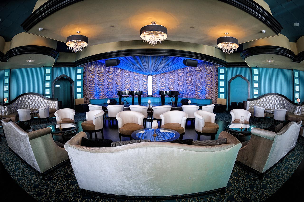 Elegant lounge with curved white chairs, tufted sofas, and a blue stage backdrop.