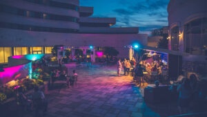 Rooftop patio at night with guests, colorful lighting, and bar service