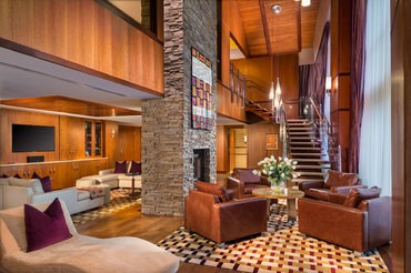 The elegant Presidential Suite at The Lodge showing the sitting room with leather arm chairs, plush couches, a fireplace, and spiral staircase with large windows overlooking the great lawn