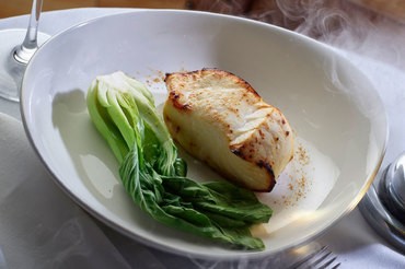 Steaming grilled black cod plated with leafy greens