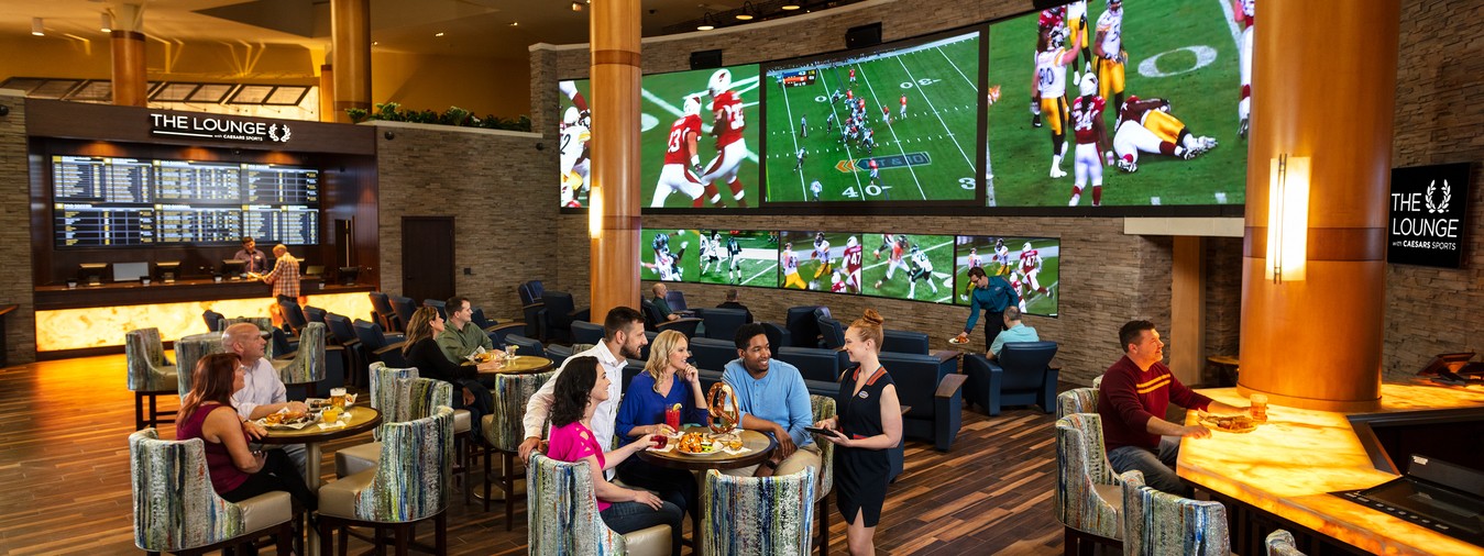 Overview of tables and chairs with people eating and watching football on 3 big screens