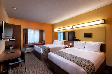 Room with two queen bed side by side, a desk, television, and a window nook at Sandstone Hollow Inn