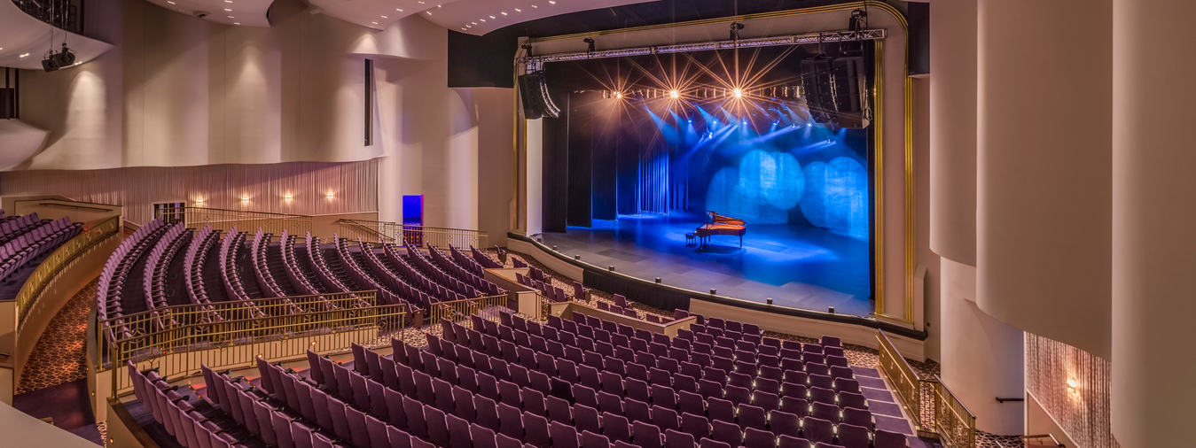 empty theater seats with blue spot lights and piano on stage