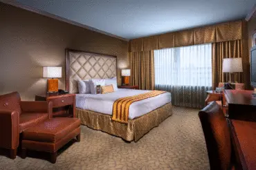 A deluxe suite at The Hotel at Turning Stone with a king bed, wooden desk, leather arm chair, and seperate sitting room
            