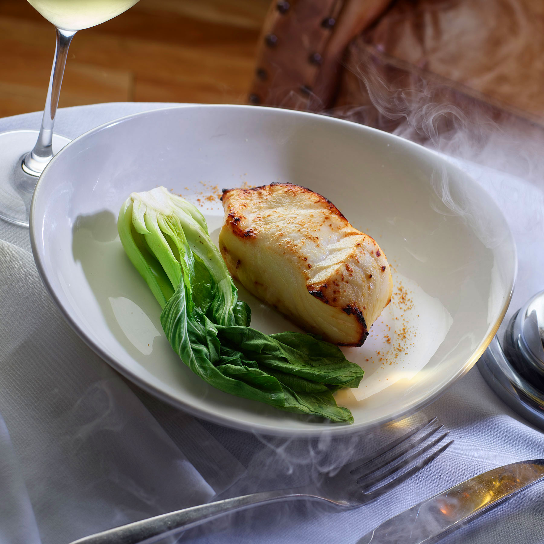 Steaming grilled black cod plated with leafy greens