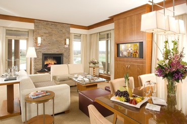 An expansive and bright living room in the VIP Suite at The Lodge at Turning Stone with a roaring fireplace and big windows overlooking central new york
