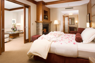 A single king bed covered in flower petals in the deluxe suite at The Lodge with a fire in the fireplace