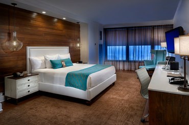 Floor to ceiling windows behind a luxurious king-sized bed in a deluxe room in the high rise Tower at Turning Stone Resort Casino