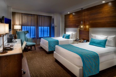 Floor to ceiling windows behind two queen-sized beds in a deluxe room in the high rise Tower at Turning Stone Resort Casino