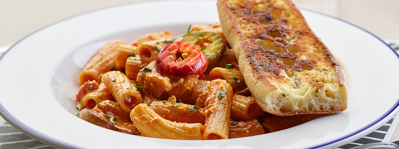 Rigatoni marinara with garlic bread on a white plate served at Seven Kitchens